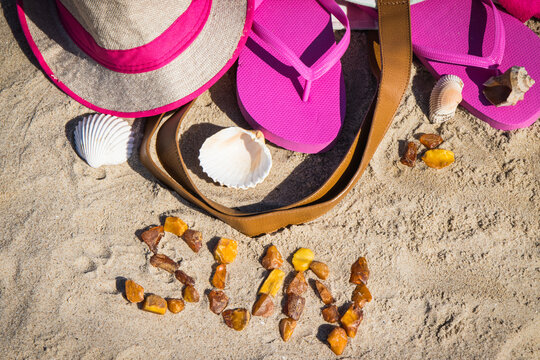 Inscription sun made of amber and different accessories for relax on sand. Straw hat, slippers and towel. Summer time on beach