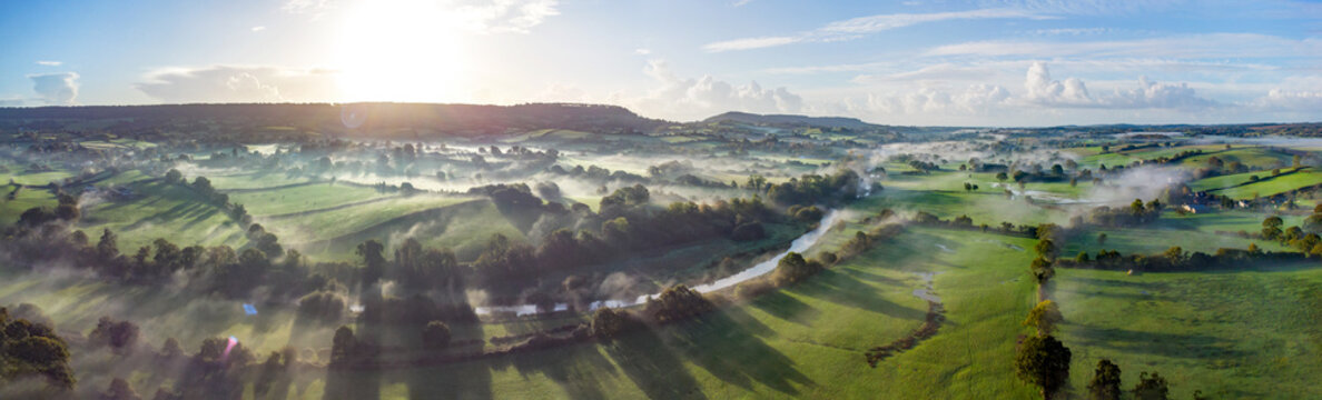 Aerial panorama picture of the river Otter near Honiton and Ottery St Mary. Sunrise and rolling mist cross the lush green fields below. Spectacular landscape. 