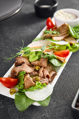 Gourmet meat selection elegantly displayed with slices of roast beef, sumptuous chicken or turkey, and melt-in-your-mouth duck, enhanced with vibrant greens, tangy tomatoes, and a creamy accompaniment