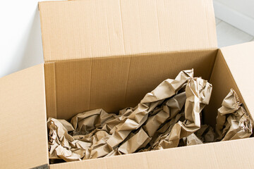 Cardboard box with crumpled paper, paper filling inside for packaging goods from online stores, eco friendly packaging made of recyclable raw materials in light interior