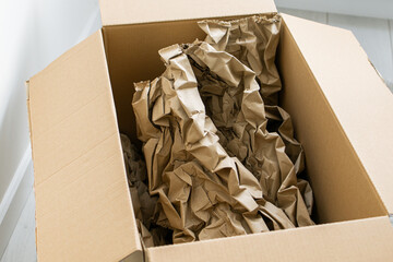 Cardboard box with crumpled paper, paper filling inside for packaging goods from online stores, eco friendly packaging made of recyclable raw materials in light interior
