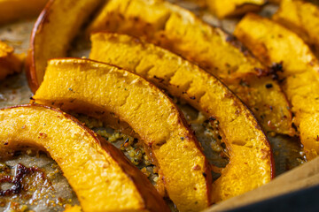 Tasty grilled, roasted pumpkin Slices with olive oil, herbs and salt freshly from oven on a backing paper, parchment sheet on Baking Tray. Close up.