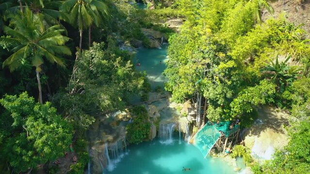 Cambugahay falls, Siquijor island, Philippines. Slow aerial travelling. Cinematic drone view. Filipino tourists swimming and playing in the turquoise waterfall lagoons. Famous travel destination.