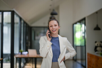 Fototapeta premium Smart businesswoman stands talking on the phone at the table in the office.