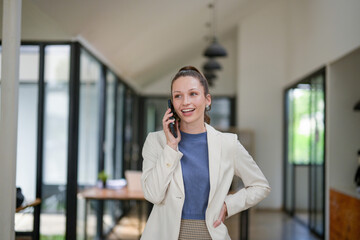 Obraz premium Smart businesswoman stands talking on the phone at the table in the office.