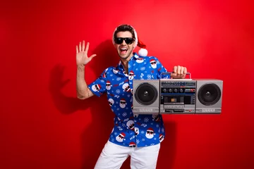 Tuinposter Photo of young positive guy wear cool sunglasses macho listen vintage cassette player raised palm up isolated on red color background © deagreez