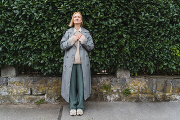 Naklejka premium Woman with eyes closed on background of green leaves wall. Concept of outside of office, Work-Life-Balance, Taking Break.