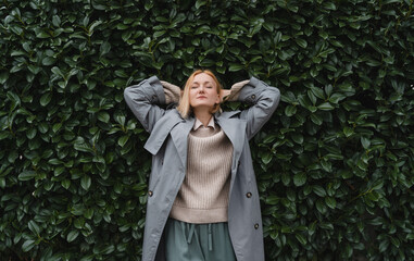 Woman with eyes closed on background of green leaves wall. Concept of outside of office, Work-Life-Balance, Taking Break.