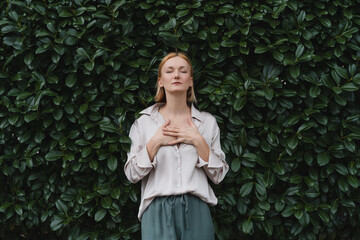 Woman with eyes closed on background of green leaves wall. Concept of outside of office, Work-Life-Balance, Taking Break.