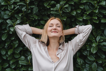 Woman with eyes closed on background of green leaves wall. Concept of outside of office,...