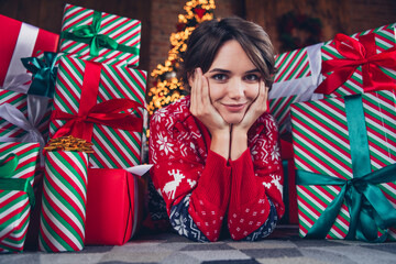 Photo of lovely young lady lying floor hands cheeks gift pile dressed stylish red sweater christmas...