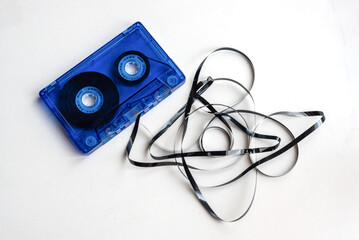 Primer plano de una antigua cinta de casete de audio azul con la cinta magnética fuera y enredada sobre fondo blanco.
