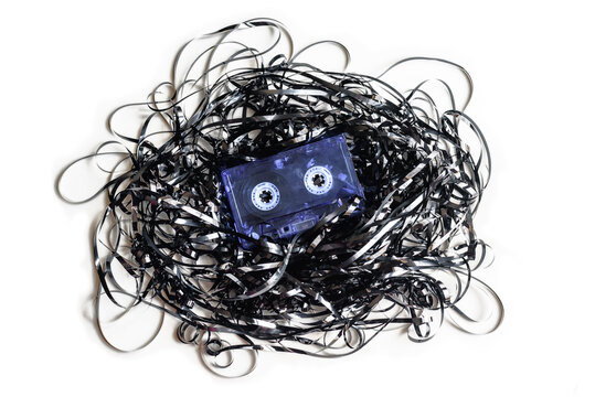 Antigua cinta de casete de audio con toda la cinta magn&eacute;tica fuera y enredada sobre fondo blanco.