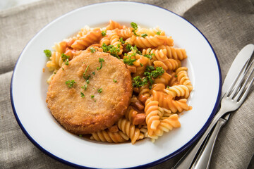 Jägerschnitzel nach DDR GDR Rezept mit Jagdwurst paniert, Spirelli Fusilli Nudeln, Tomatensoße, Petersilie auf Emaille Teller, Besteck und grauer Leinen Serviette