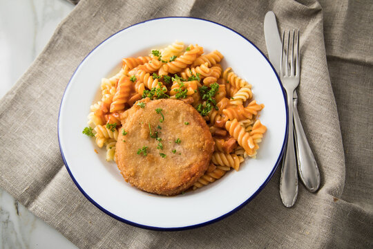 J&auml;gerschnitzel nach DDR Rezept mit Jagdwurst paniert, Spirelli Fusilli Nudeln, Tomatenso&szlig;e, Petersilie auf Emaille Teller, Besteck und grauer Leinen Serviette
