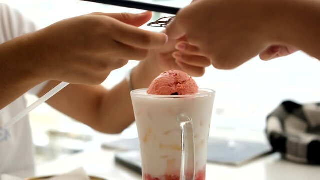 woman's hand is eating a cold milk drink with a scoop of strawberry ice cream on top.