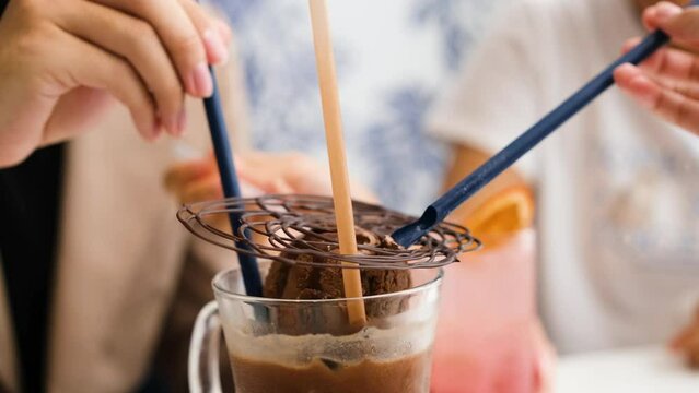 woman's hand uses a straw spoon to eat an iced cocoa drink with a scoop of chocolate ice cream and toppings placed on top