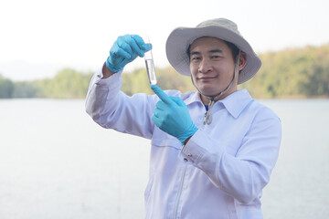 Asian man environment researcher holds tube of sample water to inspect from the lake. Concept,...