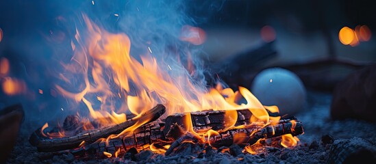 Close up bonfire with vivid burning firewood orange flame blue smoke glowing embers and bright sparks in bokeh background