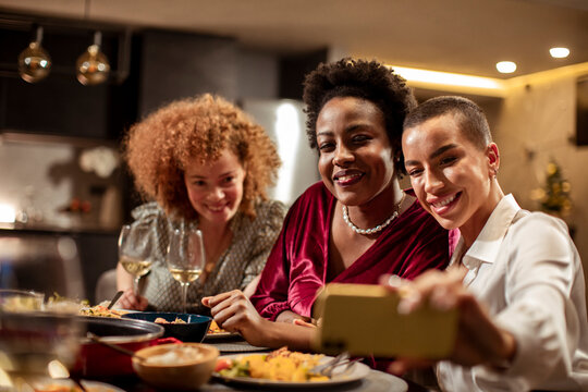 Young female friends taking a selfie on a smartphone during a dinner in the kitchen