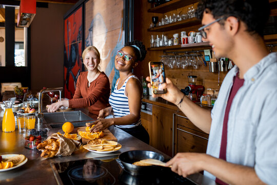 Young man taking a picture of his roommates in the kitchen - Powered by Adobe