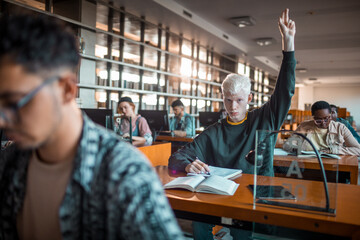 Young male student raising his hand to ask a question during lecture in the library