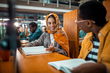 Young Muslim woman talking to a friend in a university library