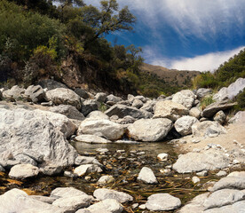 narrow creek of fresh mountain water surrounded by rocks and a green forest 