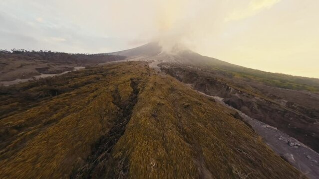 Aerial view black frozen rocky lava magma in smoke canyon foot large active erupting volcano steam over crater. Scenery wild nature gray landscape morning mountains valley natural disaster concept 4k