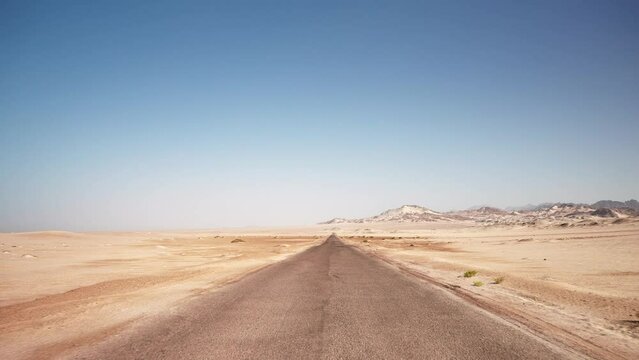 First person view of motion by empty road through the wild desert. Clear blue sky and mountains on the horizon
