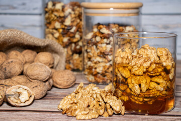 Jar full of walnuts with honey surrounded by whole and peeled walnuts
