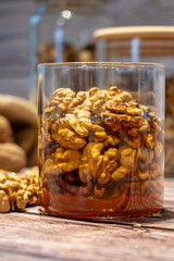 Jar full of walnuts with honey surrounded by whole and peeled walnuts