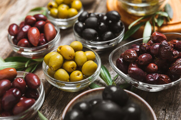 A set of green, red and black olives on  background. Various types of olives in bowls and fresh olive leaves. Vegan. Olive fruits. Place for text. Copy space