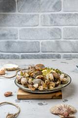 Vongole prepared clams lie in a plate on a light background against a gray brick wall, free space, vertical photo