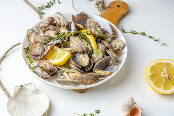 Healthy appetizer of steamed vongole clams served in a white plate with lemon and herbs