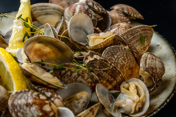 Vongole clams with lemon and herbs close-up, dark background.