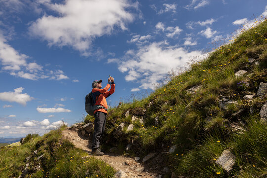 Man with backpack standing on trail with taking pictures of further route against the background of picturesque sky