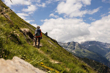 Fototapeta na wymiar Gray-haired man with backpack climbing steep slope against bright sky and mountain range, Austria