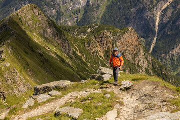 Adult man with backpack standing on steep rocky trail and looking at camera on background of alpine...
