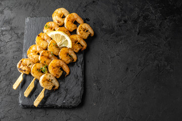 Skewers with grilled shrimp with lemon and spices on a dark table, background. Top view, free space