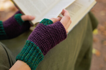 The girl turns the page of the book in knitted gloves outdoors