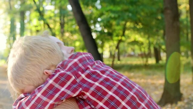 Close-up video portrait of a mother and son during a walk in the autumn park. Woman holds her toddler son in her arms and hugs him tenderly. A little boy is having fun and fooling around with his mom.