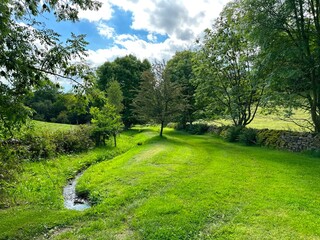 Rural landscape, with a small stream, fields, dry stone walls, and old trees, close to the, Aire Valley Road, Keighley, UK