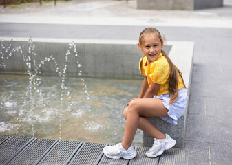 little girl playing with small fountains in the town square on a hot summer day.