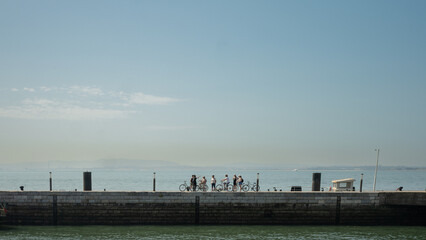 Lisbon, Portugal - May 25, 2023: Silhouettes of a group of bicycle riders by the Tagus river on a...