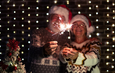 Defocused senior family couple in Santa hat celebrate together with love Christmas and new year event night firing sparklers. Man and woman enjoy magic moment relationship at Christmas time