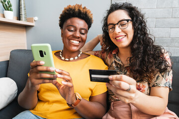 Two women make purchases online with a credit card in their living room - obrazy, fototapety, plakaty