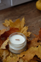 Handmade soy candle in a glass cup with a wooden wick with maple leaves. Candle with wooden wick. Scented candle for interior. Home decoration, minimal interior. Autumn