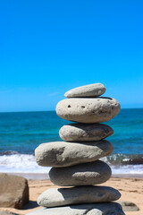 Fototapeta na wymiar Zen stone little pile on sea beach. The stones of the pyramid balance on the rock. Zen stones balance spa on beach.