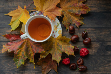 A cup of hot aromatic tea with lemon set on a wooden table covered dry autumn leaves and chestnuts. view from above